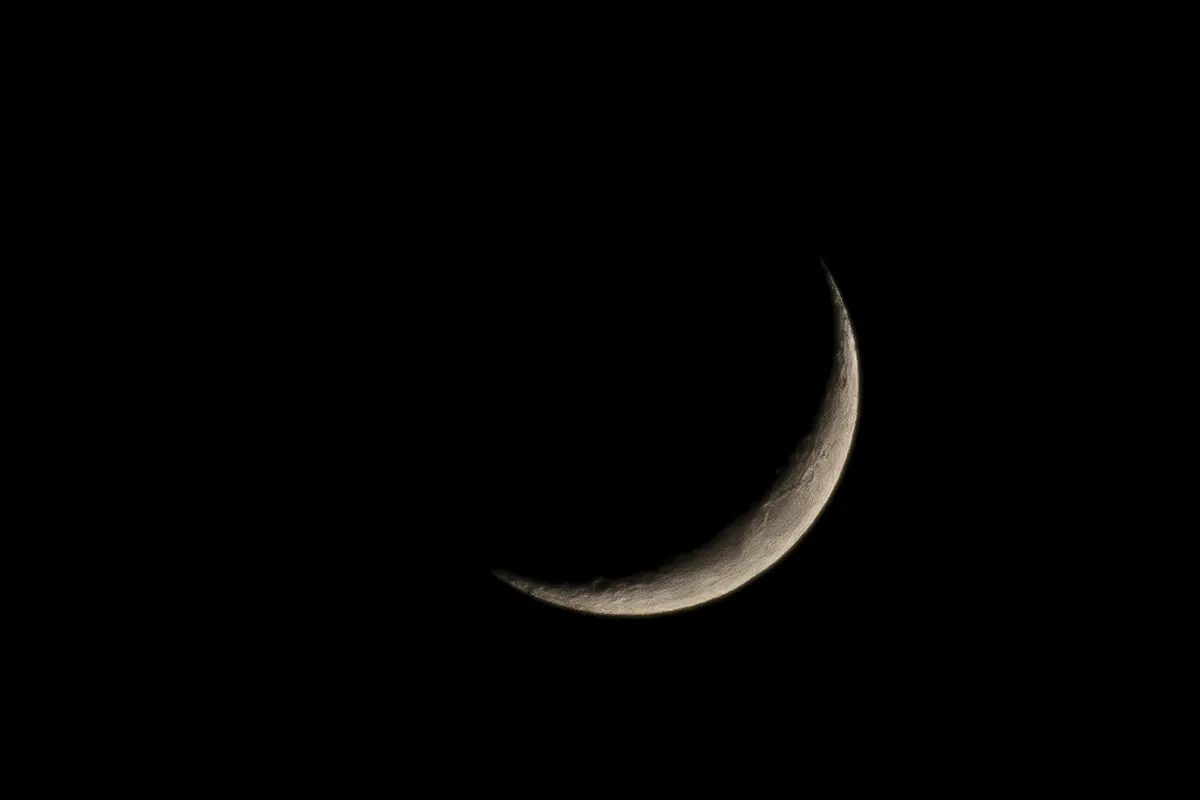 Thin crescent moon against black sky